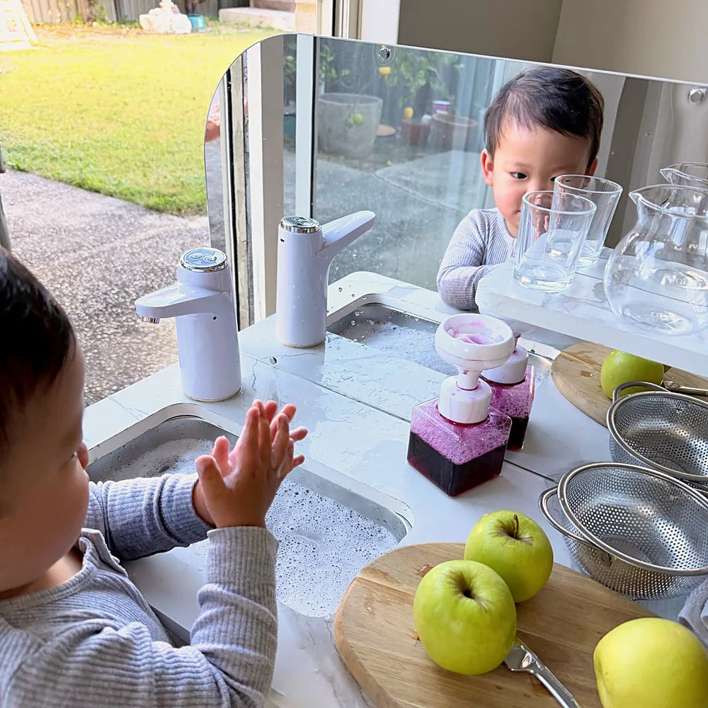 Toddler washing hands and watching himself in the mirror splashback